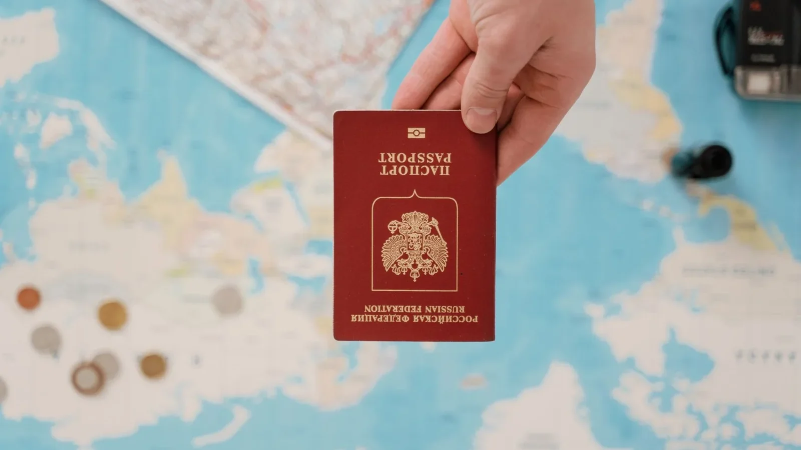 A hand holding a Russian passport above a travel-themed map, capturing world travel concepts.