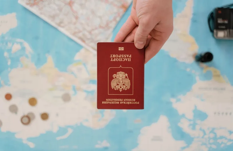 A hand holding a Russian passport above a travel-themed map, capturing world travel concepts.