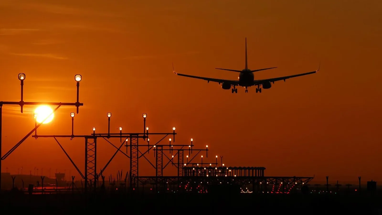 Silhouette of an airplane landing during sunset at Barcelona airport, with a vibrant orange sky.
