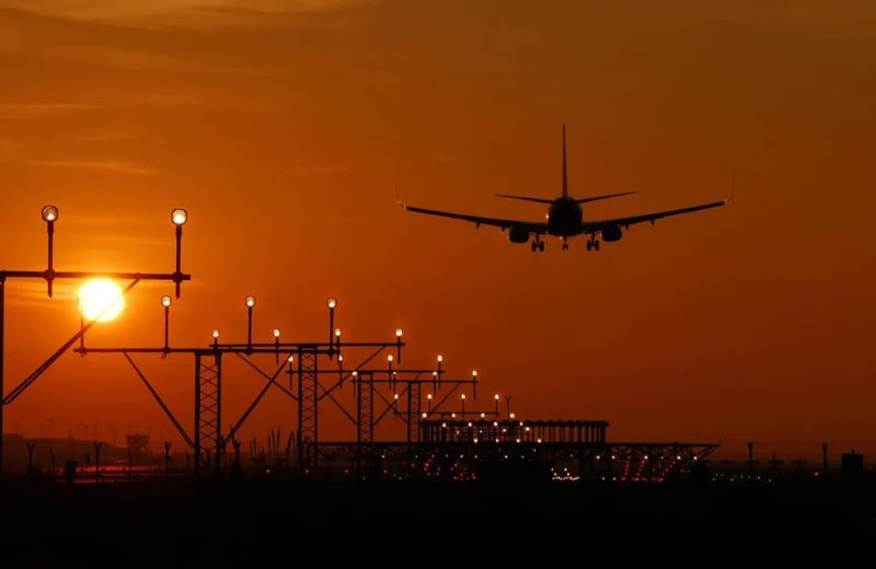 Silhouette of an airplane landing during sunset at Barcelona airport, with a vibrant orange sky.