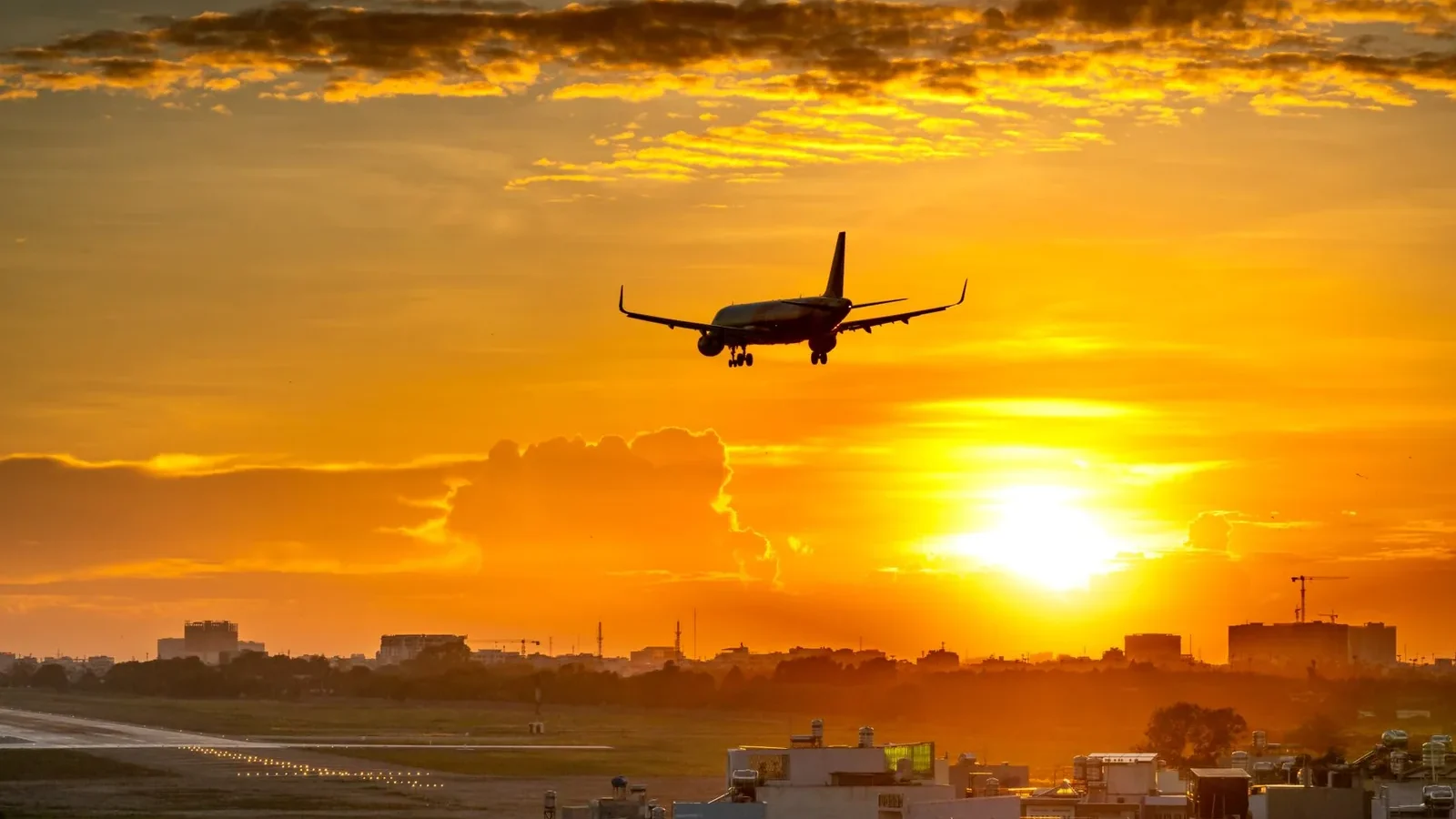 A commercial airplane lands during a vibrant sunset, creating a dramatic sky backdrop.