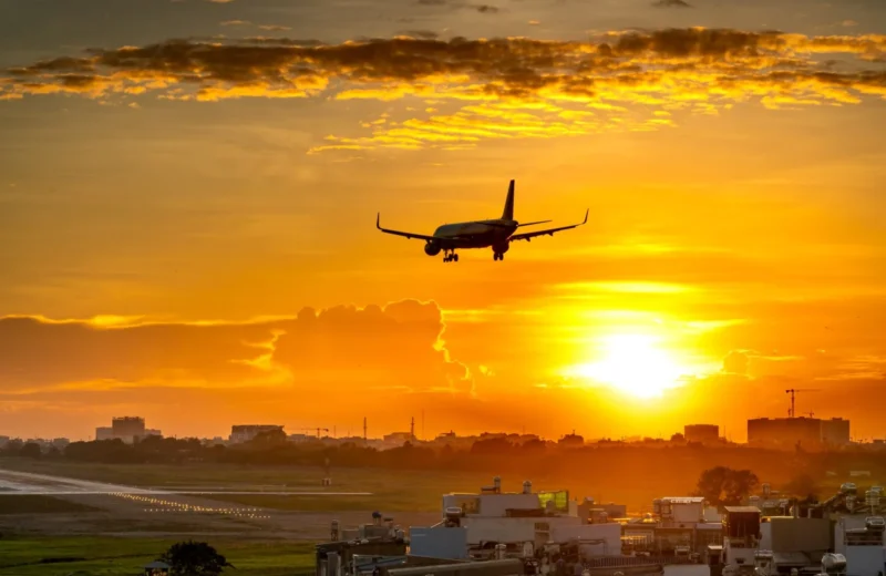 A commercial airplane lands during a vibrant sunset, creating a dramatic sky backdrop.