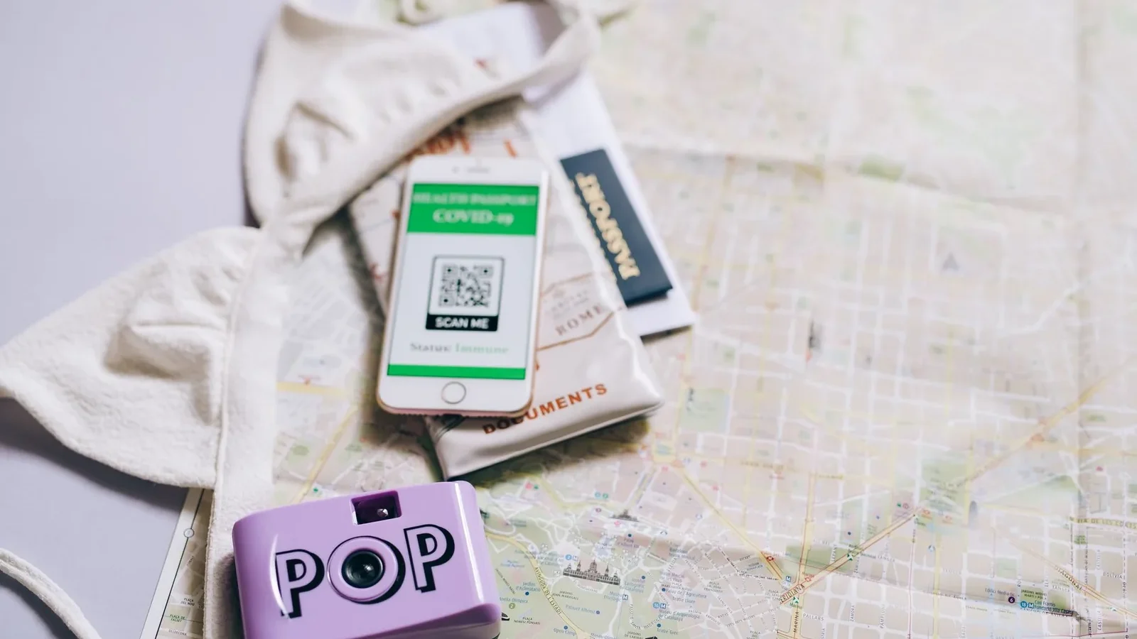 Flat lay of travel essentials including a passport, map, smartphone, and pop camera.