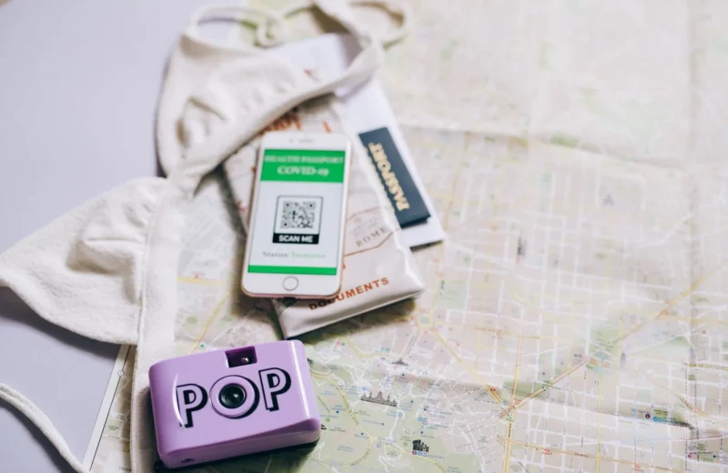 Flat lay of travel essentials including a passport, map, smartphone, and pop camera.