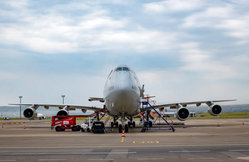 Front view of a Boeing 747 airplane at Tbilisi Airport with maintenance vehicles in the foreground.