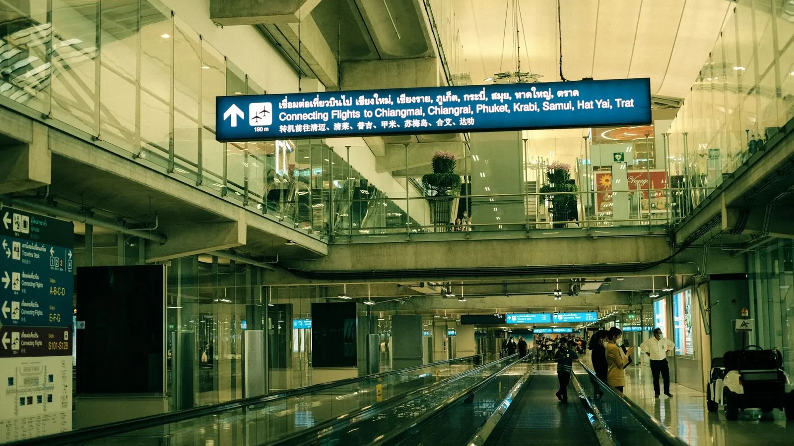 View of Suvarnabhumi Airport interior with moving walkway and signs for connecting flights.