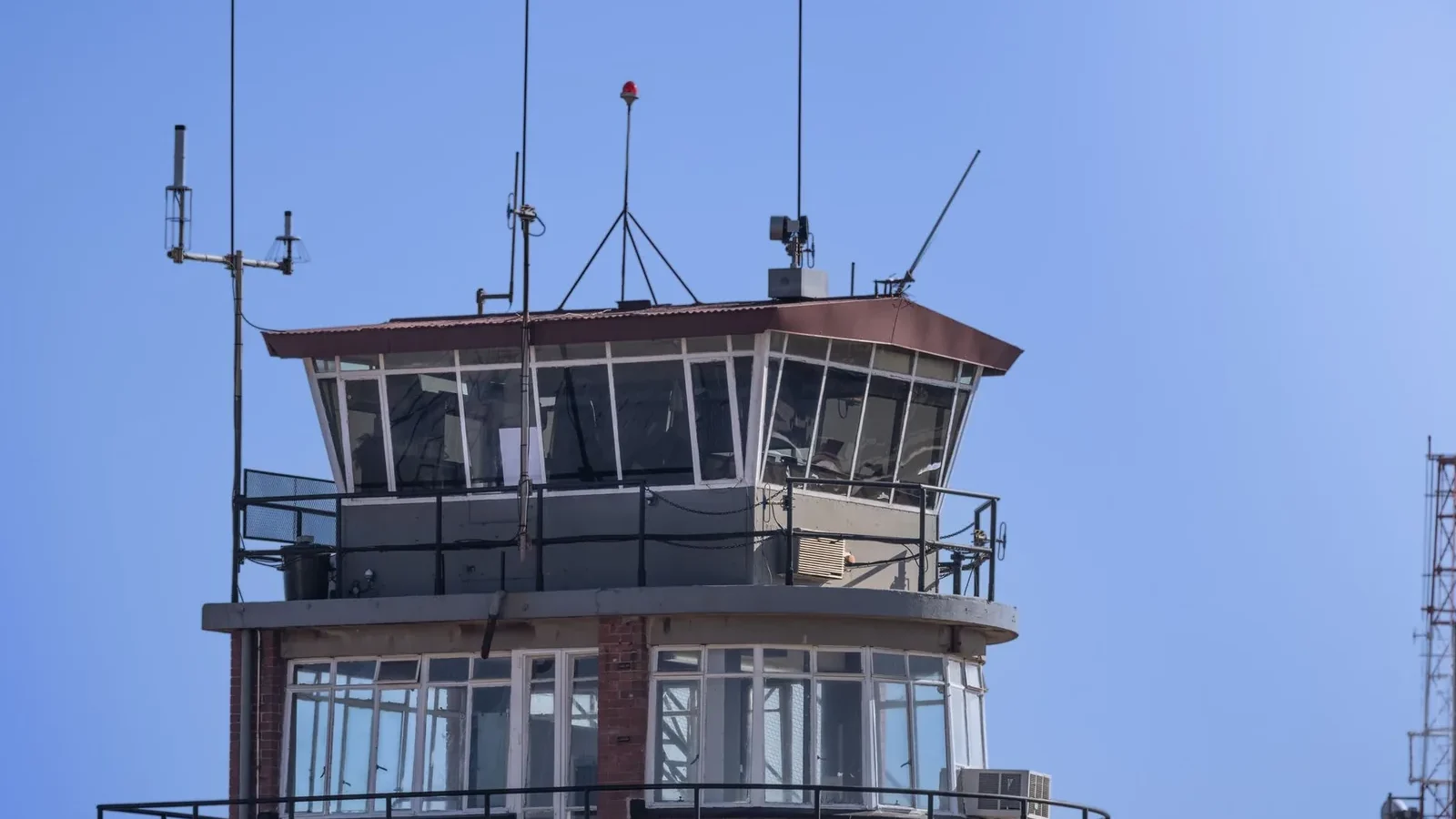A modern airport control tower against a clear blue sky, showcasing aerial communication infrastructure.