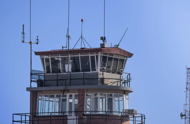 A modern airport control tower against a clear blue sky, showcasing aerial communication infrastructure.
