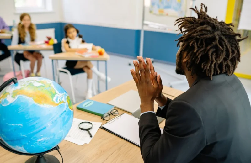 A teacher in a classroom with students, focusing on a globe for geography lesson.