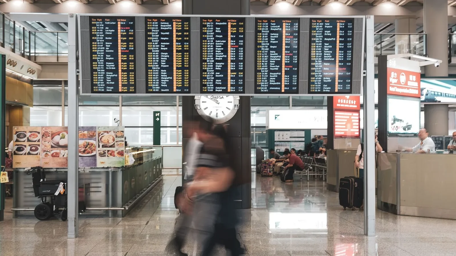 Blurred motion of travelers in a modern airport terminal with departure screens and a prominent clock.