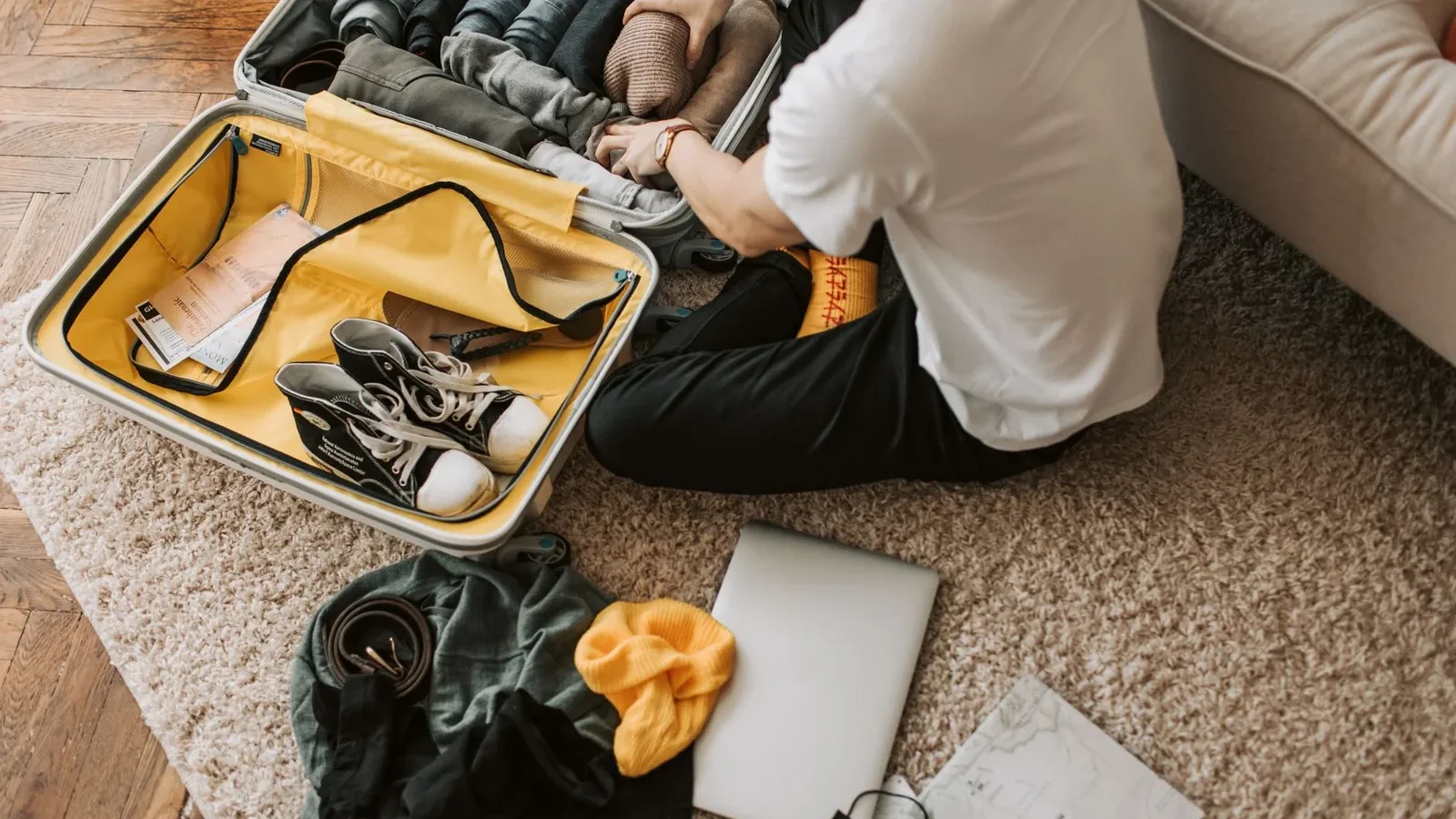 Man organizing clothes and essentials into a yellow suitcase for travel in a cozy living room.