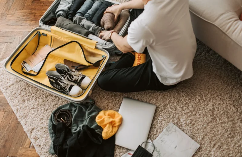Man organizing clothes and essentials into a yellow suitcase for travel in a cozy living room.
