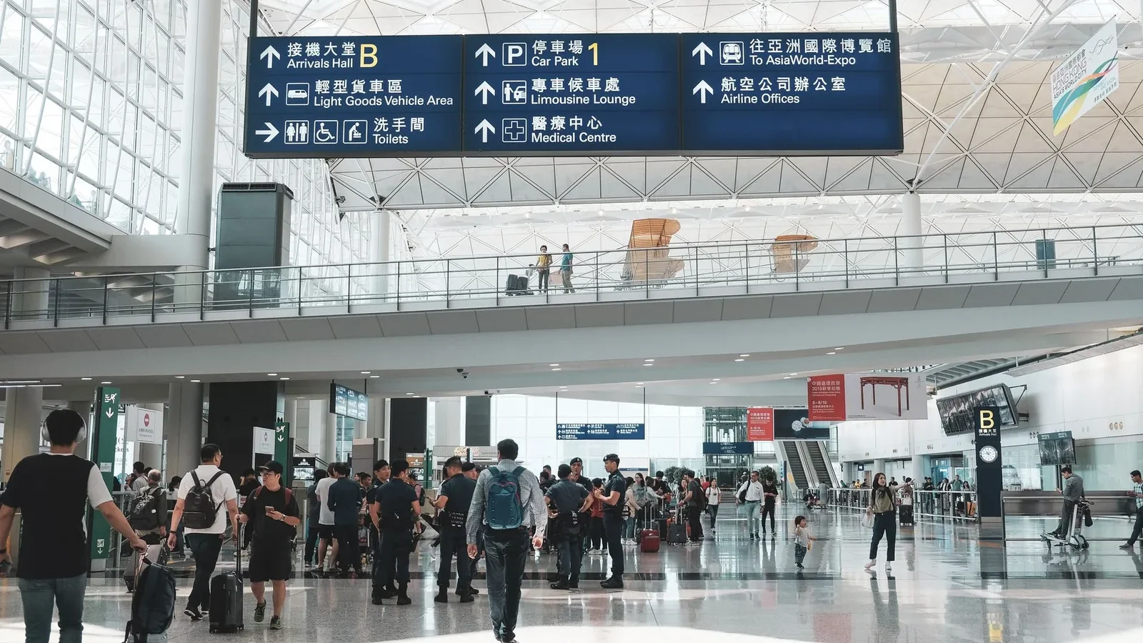 Crowded scene inside Hong Kong International Airport terminal with travelers and signage.
