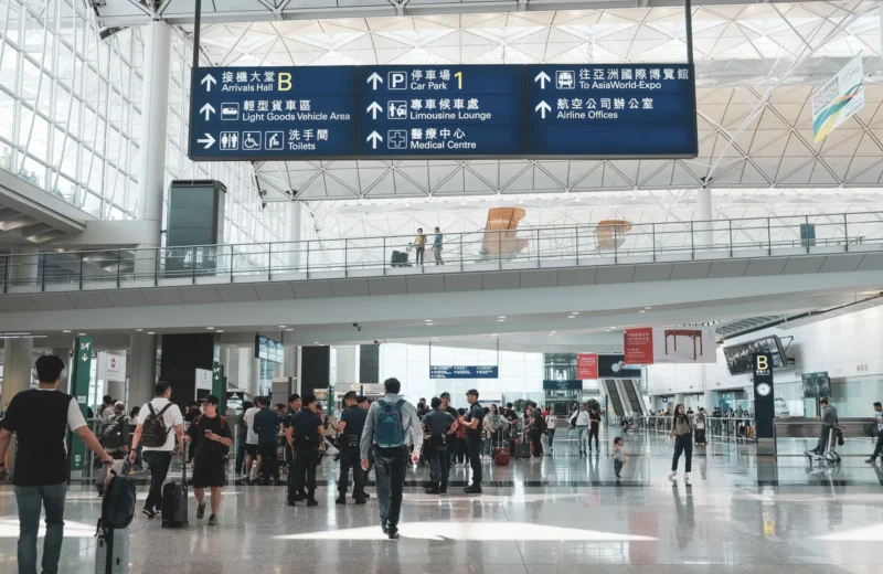 Crowded scene inside Hong Kong International Airport terminal with travelers and signage.