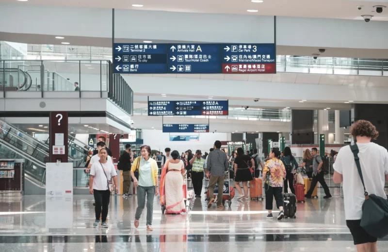 Crowded Hong Kong airport terminal with diverse passengers and informative signage.