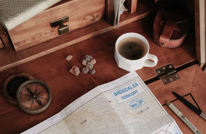 A top-down view of a rustic workspace featuring a map, compass, and a cup of coffee.