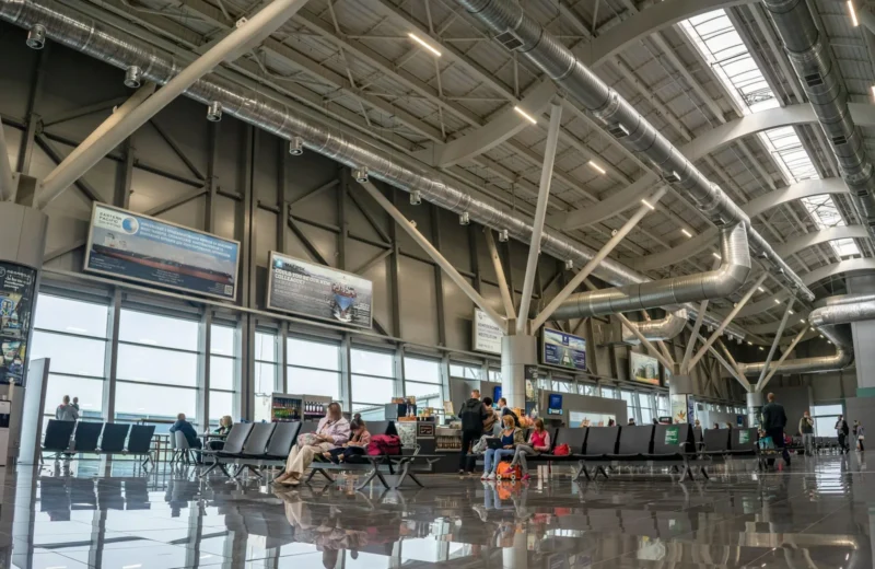 Spacious airport terminal interior with passengers seated and walking, showcasing modern design and large windows.