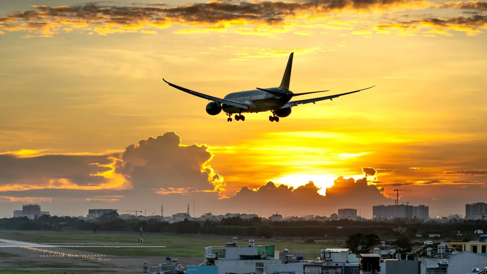 A dramatic image of an airplane landing against a vibrant sunset over a city skyline.