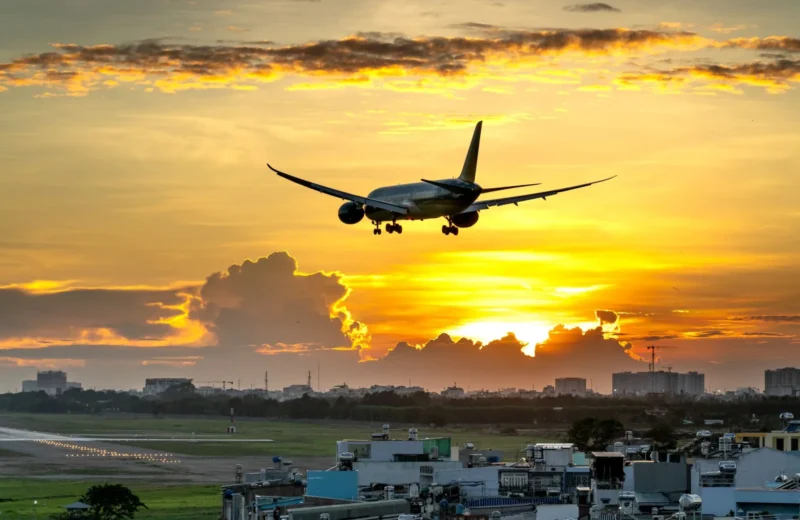 A dramatic image of an airplane landing against a vibrant sunset over a city skyline.