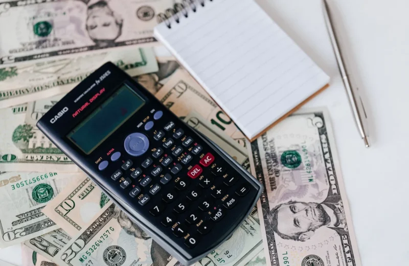 From above electronic calculator and notepad placed over United States dollar bills together with metallic pen for budget planning and calculation.