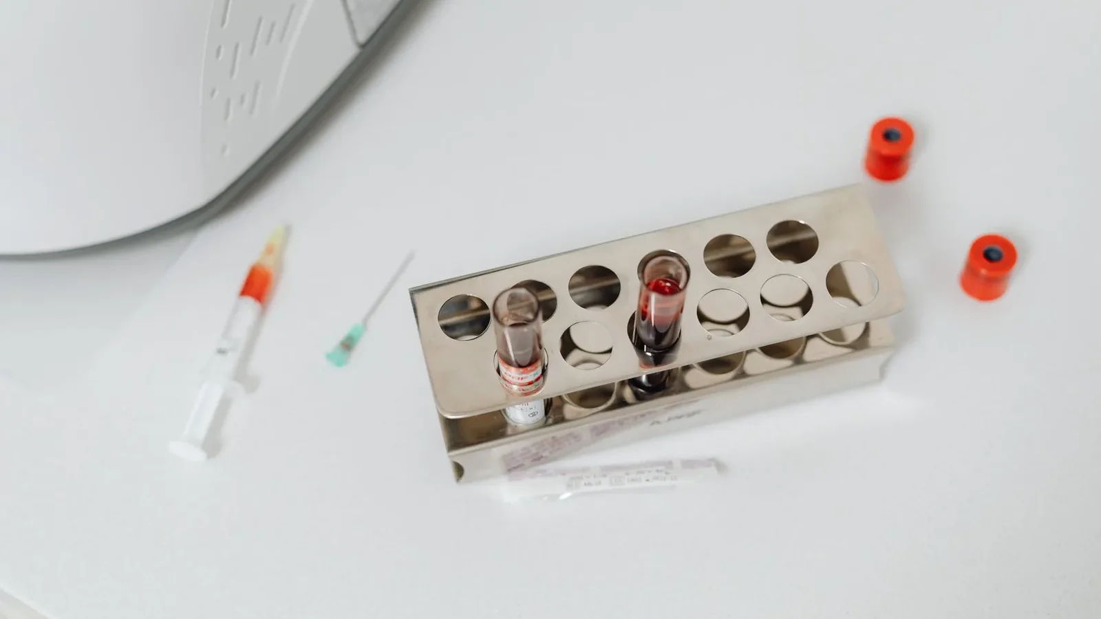 High-angle shot of lab test tubes and syringe on a white surface, perfect for science and medical themes.