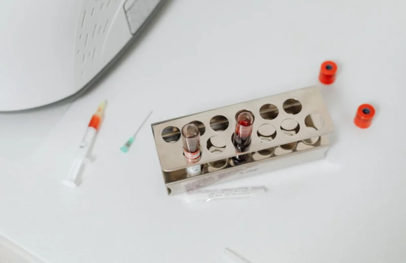 High-angle shot of lab test tubes and syringe on a white surface, perfect for science and medical themes.