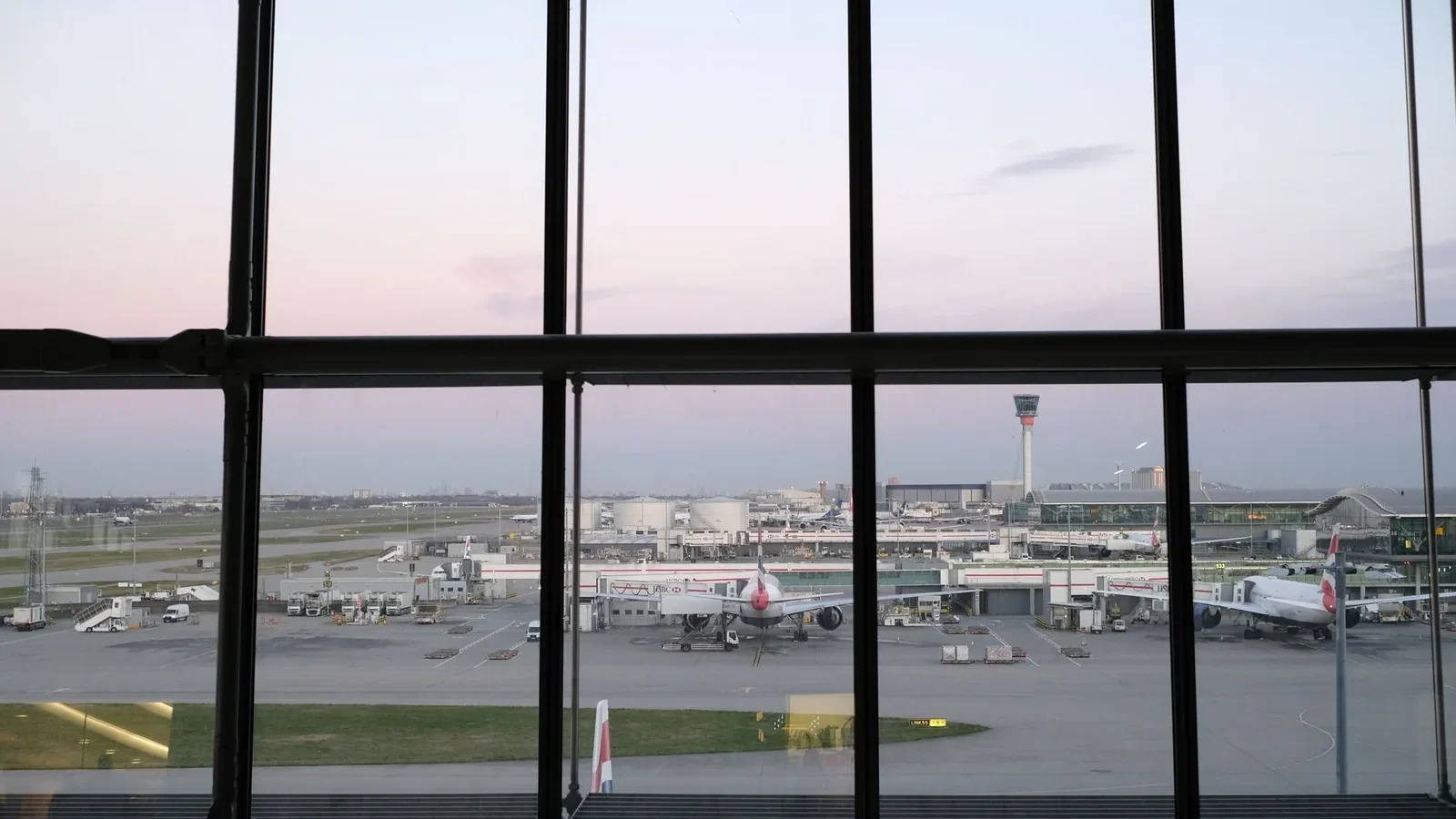 View of Heathrow Airport tarmac and airplanes through terminal window during twilight.