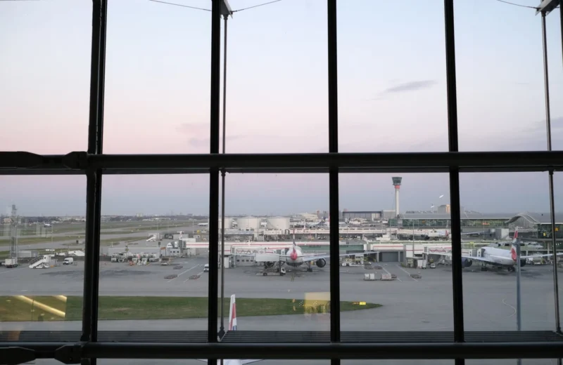 View of Heathrow Airport tarmac and airplanes through terminal window during twilight.