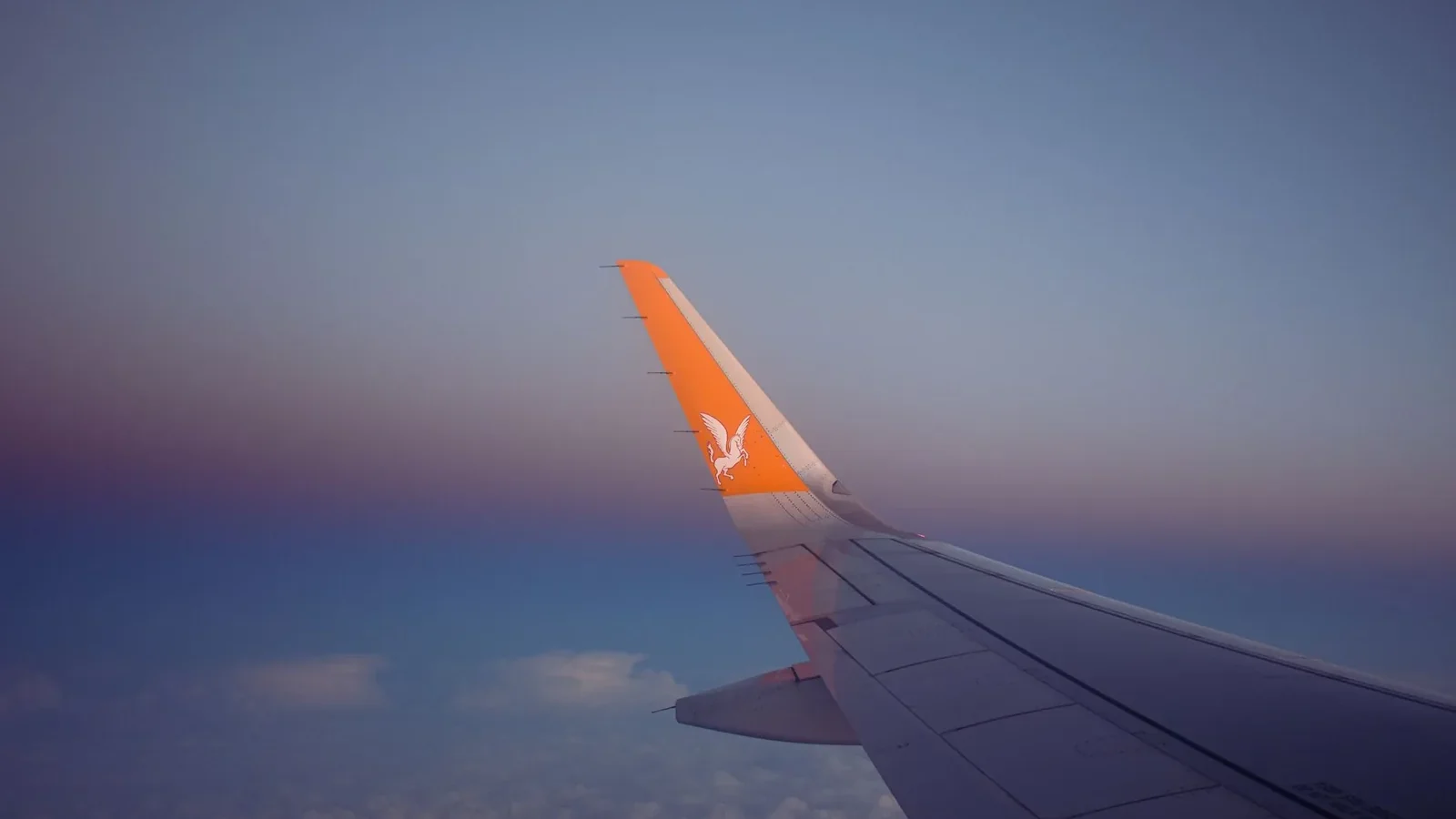 A serene view of an airplane wing soaring over clouds during sunset.