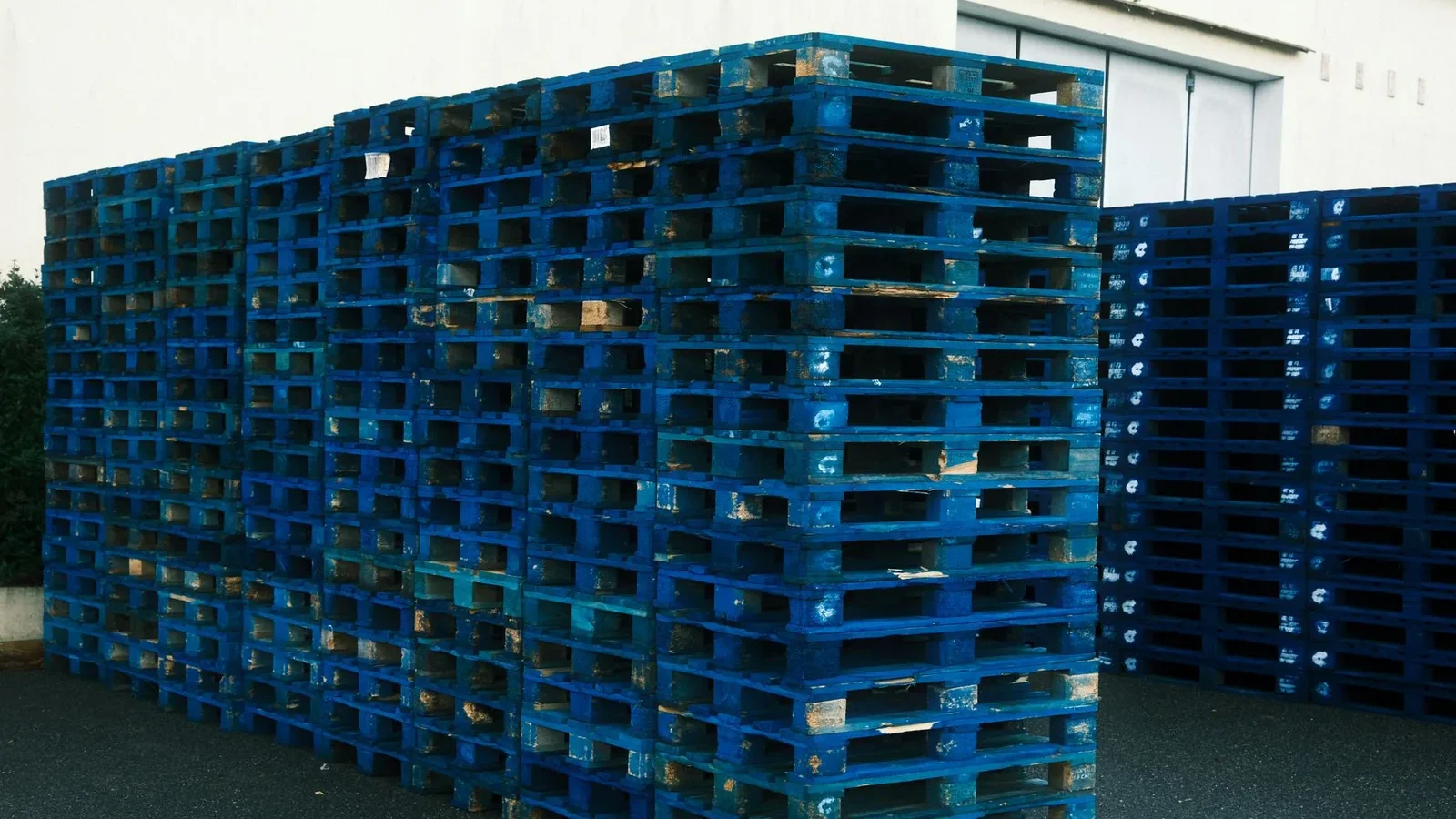 A large stack of blue pallets outside a warehouse, ideal for logistics and industrial themes.