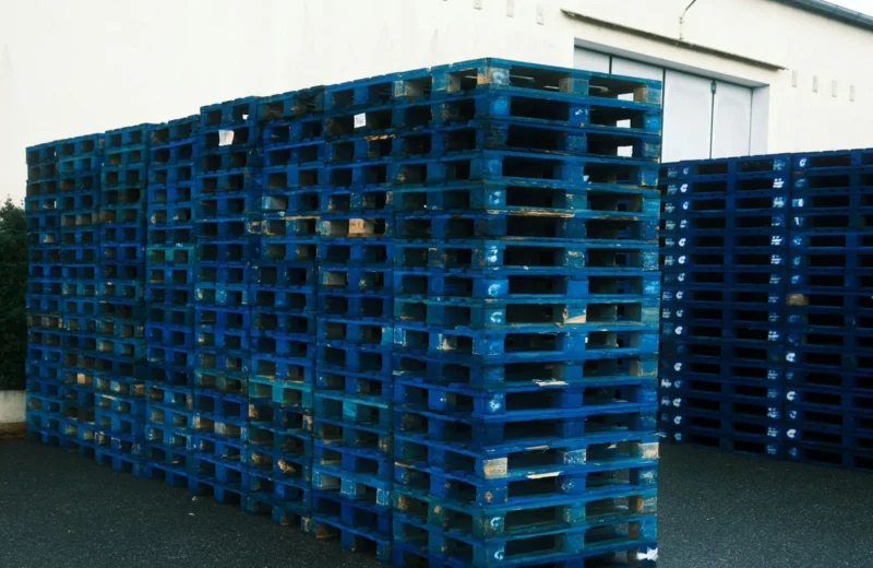 A large stack of blue pallets outside a warehouse, ideal for logistics and industrial themes.