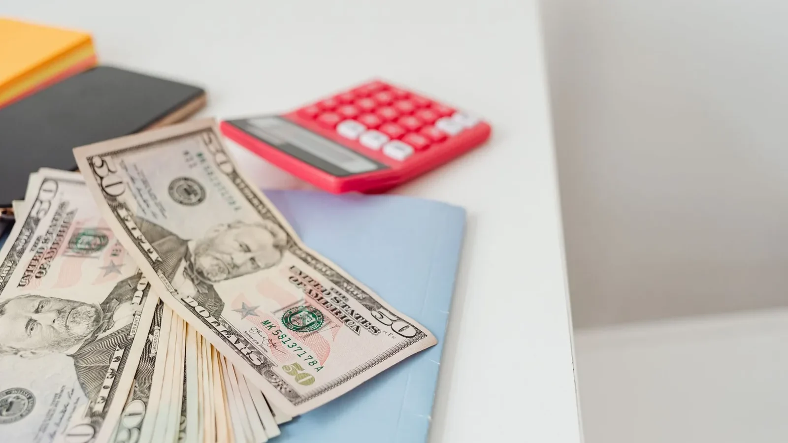 Close-up of notebooks, US dollars, and a calculator on a desk.