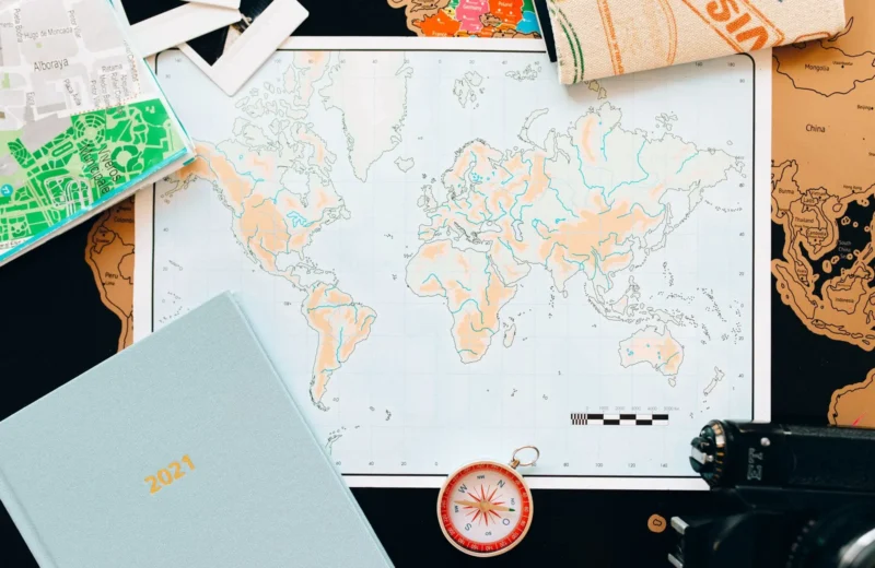 Flat lay of travel essentials including a world map, compass, and planner, perfect for planning your next adventure.