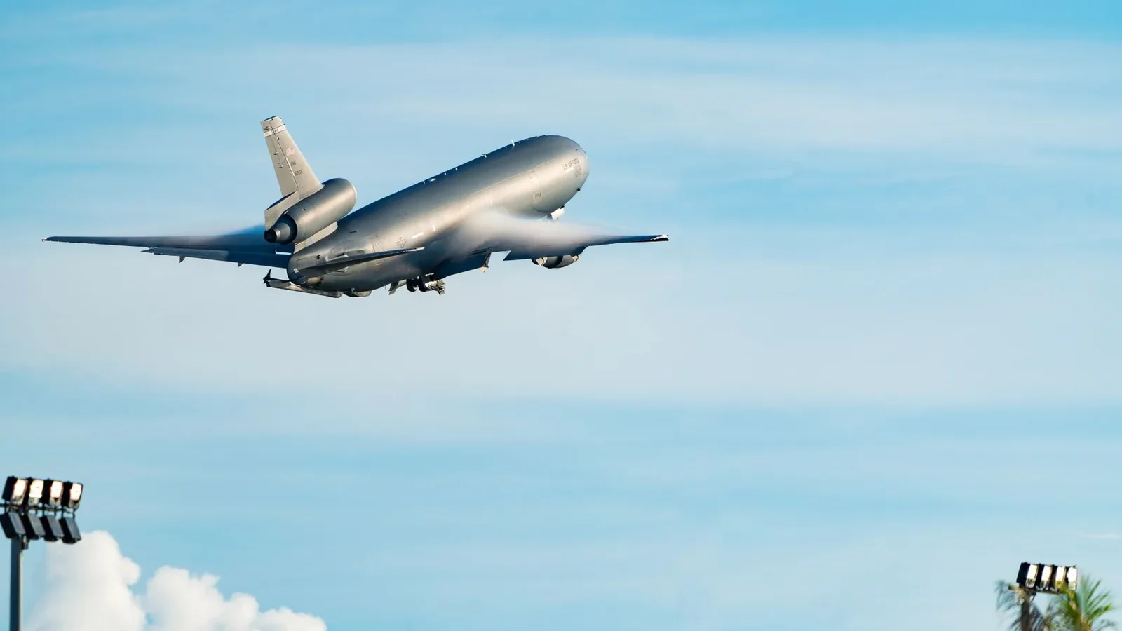A large commercial airplane ascending into a bright blue sky, surrounded by lush greenery and clouds.