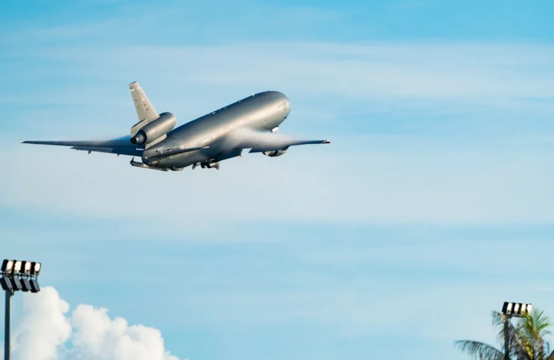 A large commercial airplane ascending into a bright blue sky, surrounded by lush greenery and clouds.
