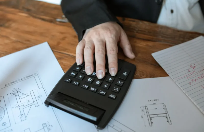 Hand using calculator for architectural calculations on blueprints.