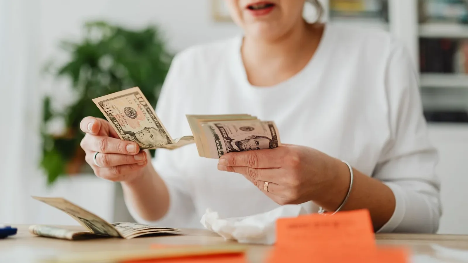 A woman sits indoors counting cash at her office desk, focusing on finances.