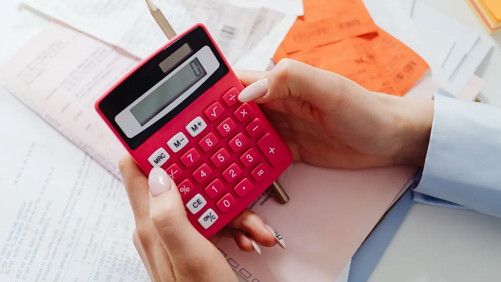 Close-up of hands holding a red calculator, managing finances with documents and receipts.