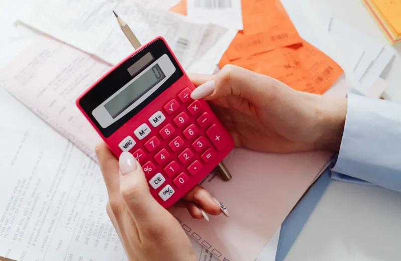 Close-up of hands holding a red calculator, managing finances with documents and receipts.