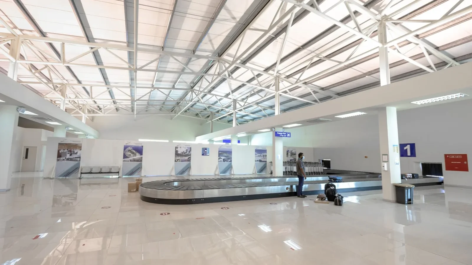 A modern and empty airport baggage claim area with a traveler waiting.
