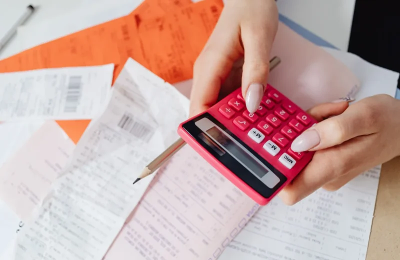 Hands using a pink calculator to manage expenses amidst various receipts and documents.