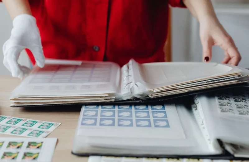 Person in red sorting a collection of vintage postage stamps using gloved hands on a wooden table.