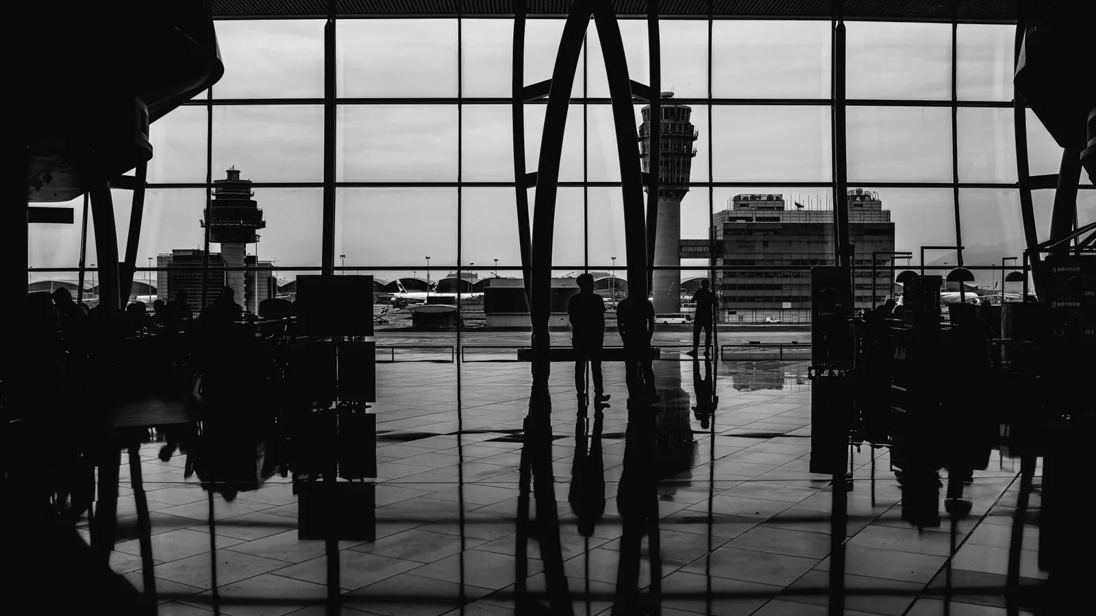 Black and white image of travelers silhouetted against large airport windows, capturing urban travel ambiance.