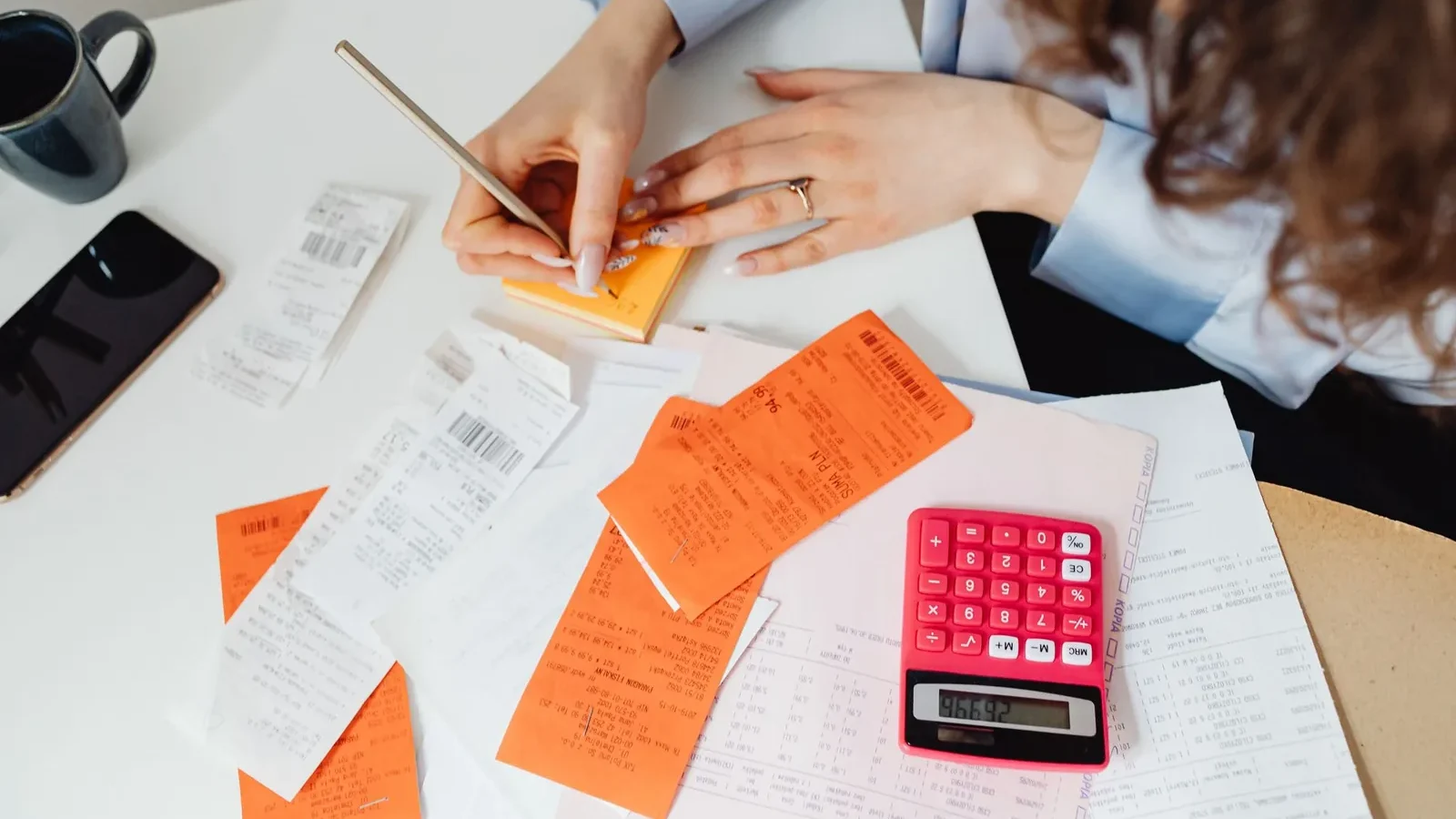 A woman writes down financial details using a calculator, receipts, and documents.