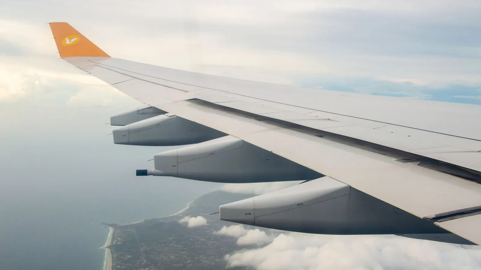 Stunning view from airplane wing showing coastline and clouds below during flight.