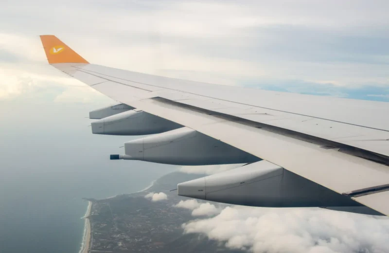Stunning view from airplane wing showing coastline and clouds below during flight.