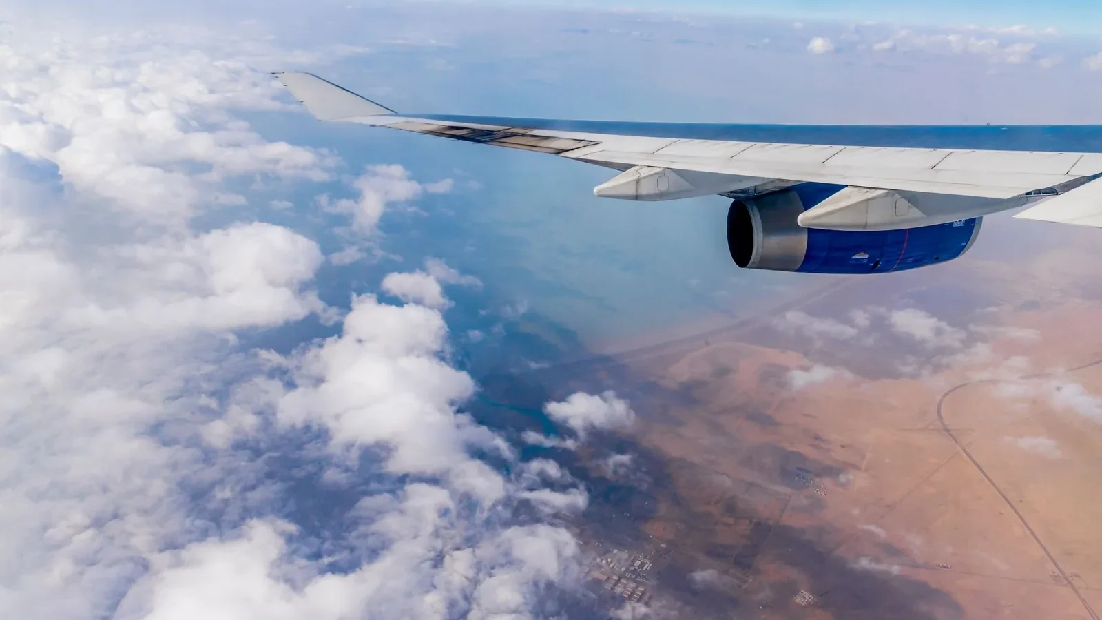 Scenic aerial view of clouds and land from an airplane window, showcasing wing and engine.