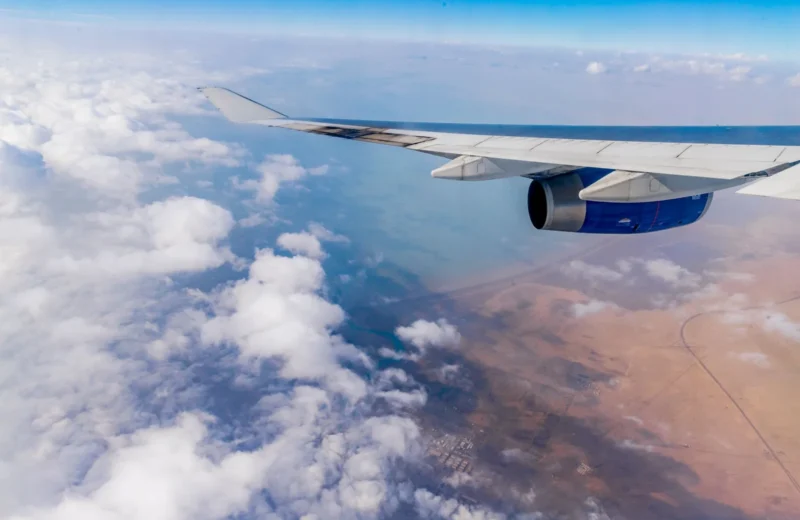 Scenic aerial view of clouds and land from an airplane window, showcasing wing and engine.