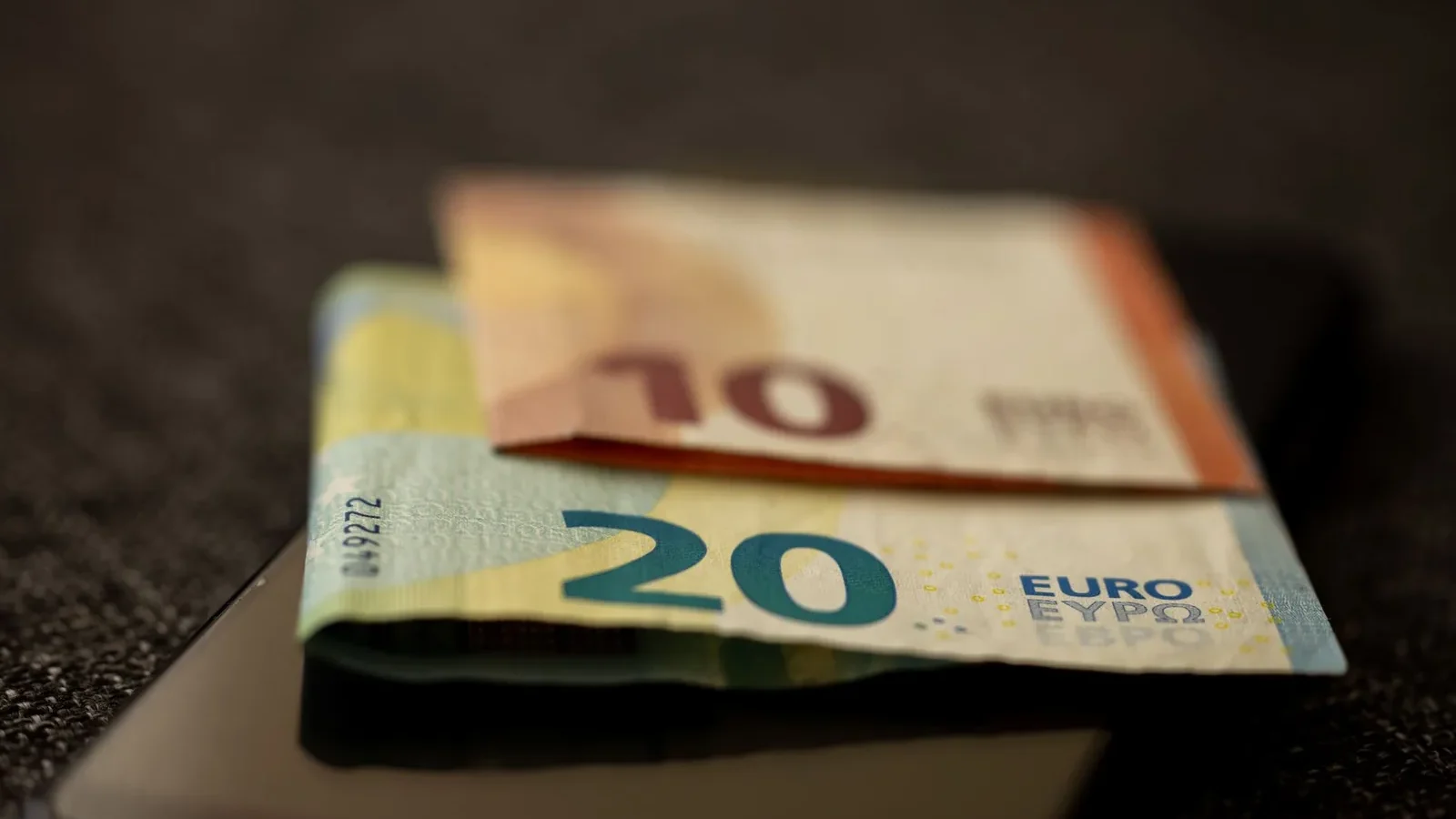 A detailed close-up shot of 10 and 20 euro banknotes placed on a smartphone, representing finance and technology.