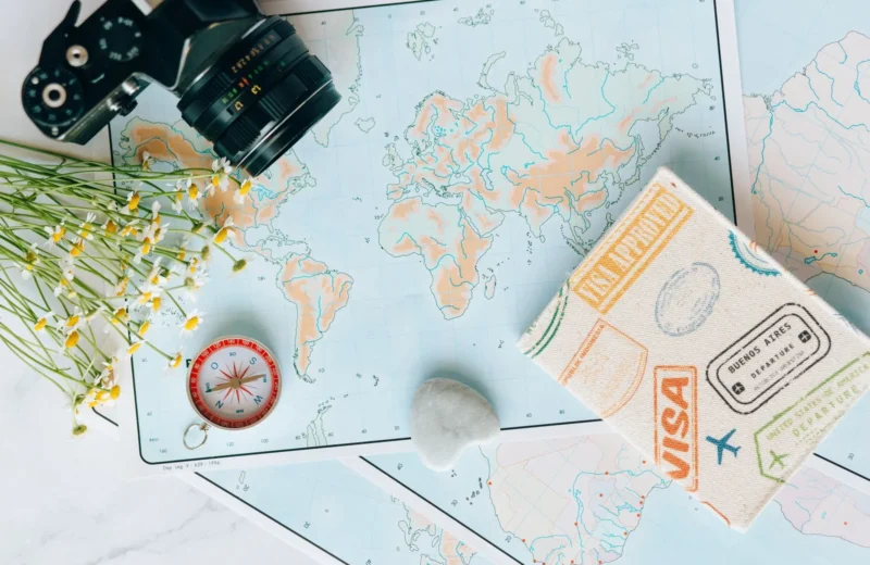 Flat lay of travel essentials: maps, camera, compass, and travel journal for planning adventures.